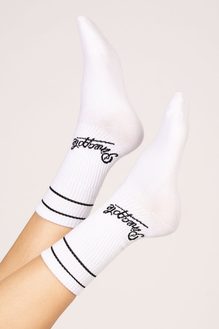 White socks with black Pineapple logo and stripes on a light beige background