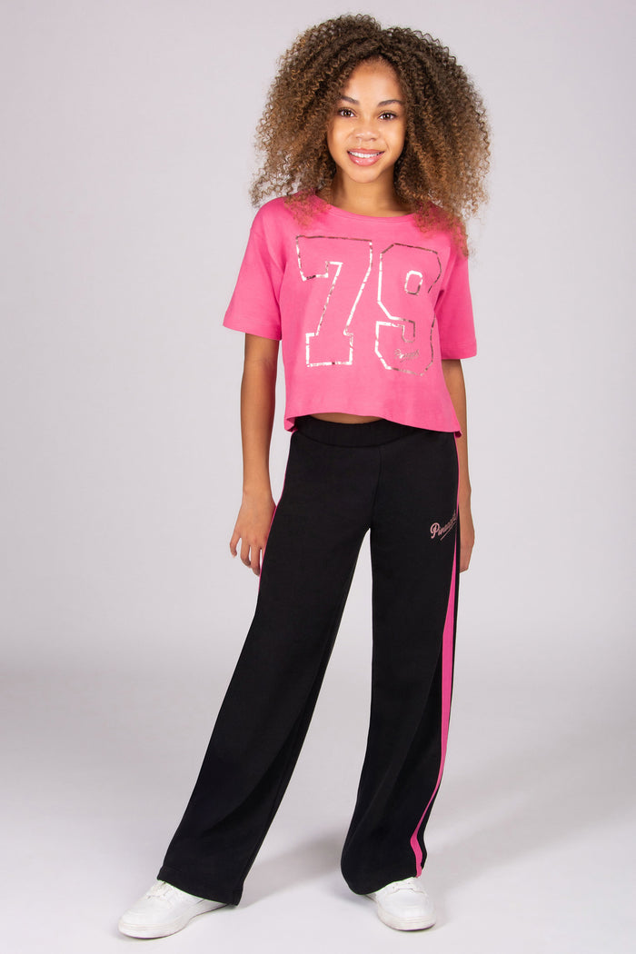 Girl wearing a pink crop t-shirt with a large number '79' and black pants with pink stripes on a white background