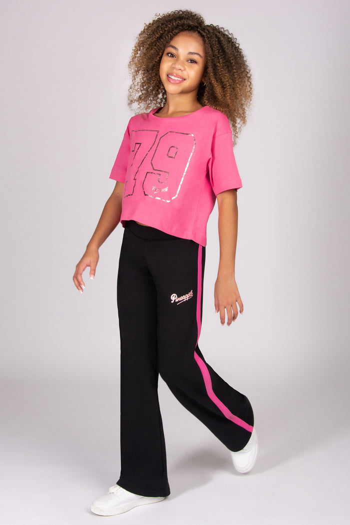 Person wearing a pink t-shirt with the number 79 and black trousers with pink paneling on a white background