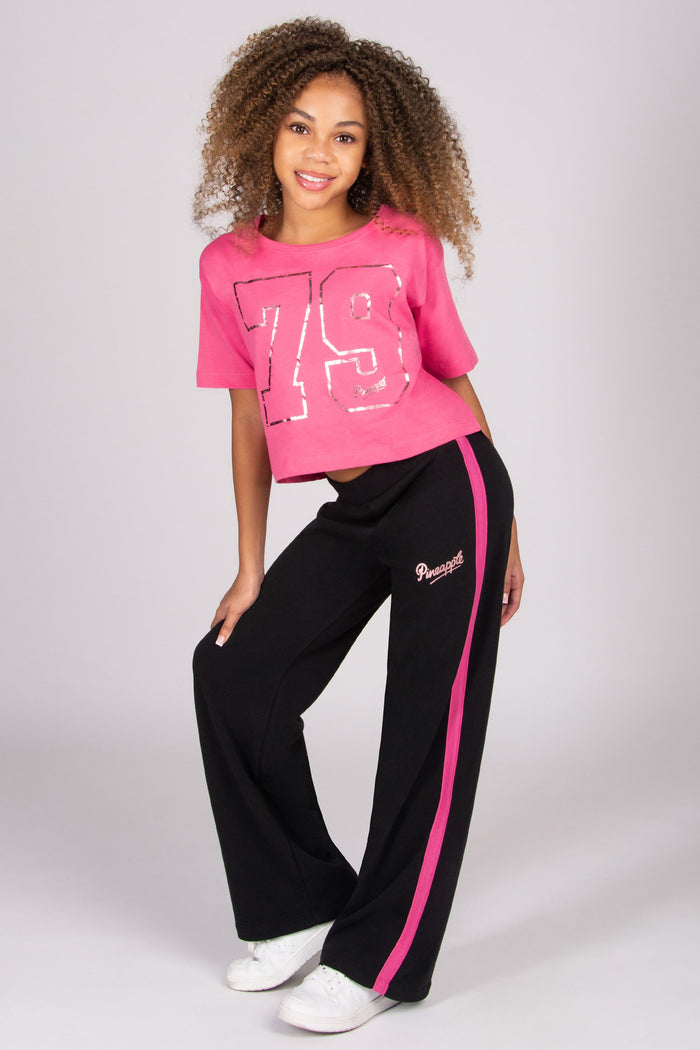 Girl wearing a pink number 79 t-shirt and black trousers with pink stripe on a white background