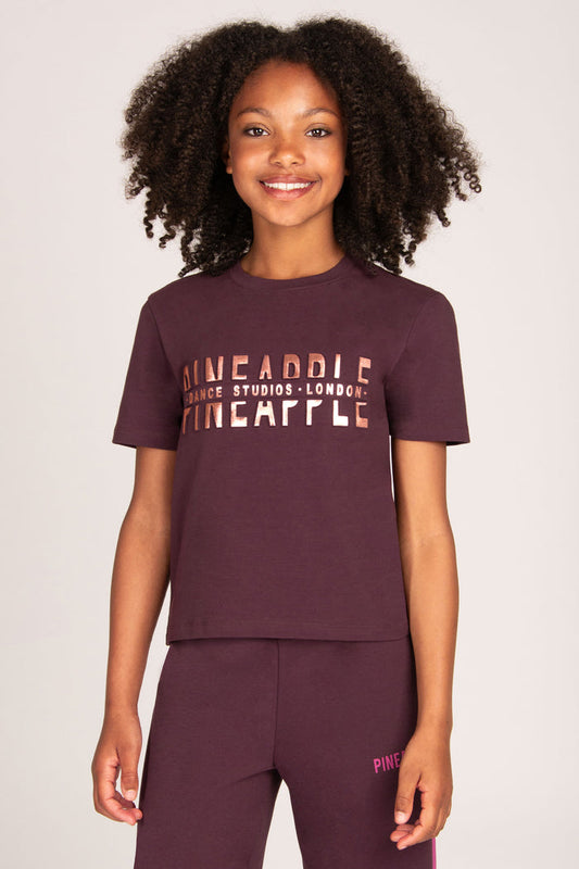 Girl wearing a maroon brown t-shirt with rose gold foil embossed 'Dance Studio London' print and matching pants on a plain background