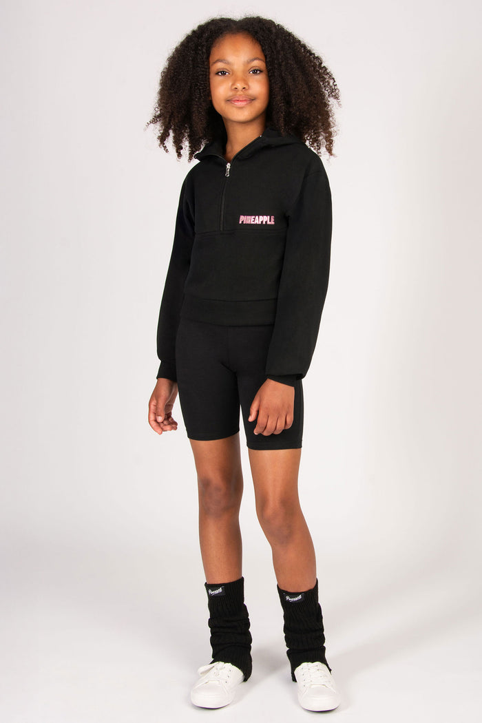 Child wearing a black hoodie and shorts set with black leg warmers on a white background