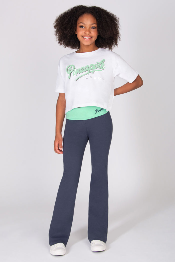 Teen wearing a white t-shirt and dark grey flared trousers on a white background
