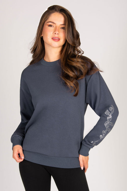 Woman wearing a dark blue sweatshirt with intricate designs on the sleeves against a plain background