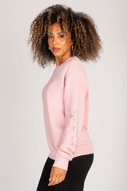 Woman wearing a pink sweatshirt with silver foil logo print on the sleeve on a plain background
