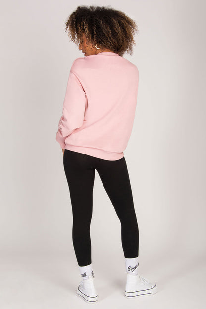 Woman wearing a pink sweatshirt, black leggings, white club socks, and white sneakers on a light grey background