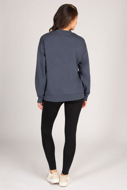Person wearing a blue sweatshirt and black leggings on a plain background