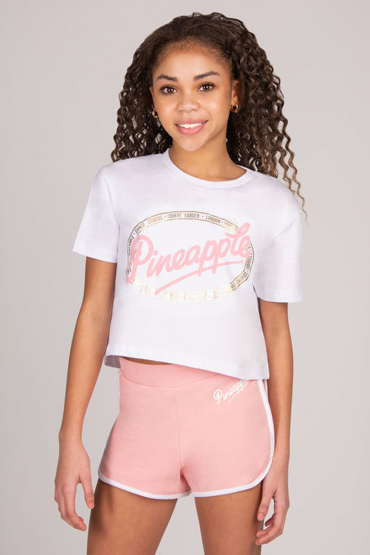 Girls wearing a white t-shirt and coral pink shorts with 'Pineapple' branding on a plain background