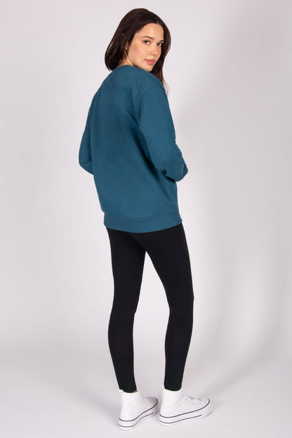 Woman wearing a teal sweater and black leggings on a white background