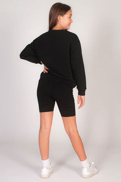 Kids' black sweater in an oversized fit paired with cycling shorts for girls.