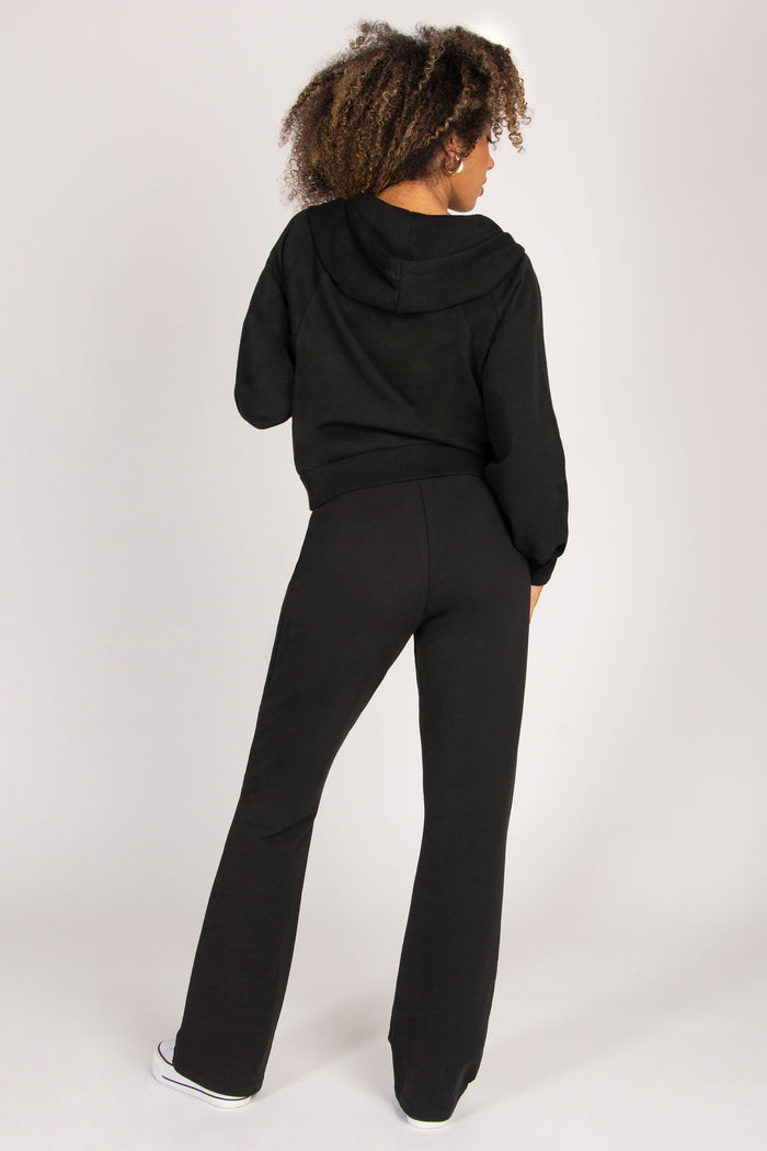 Woman wearing a black hoodie and flared joggers set on a white background