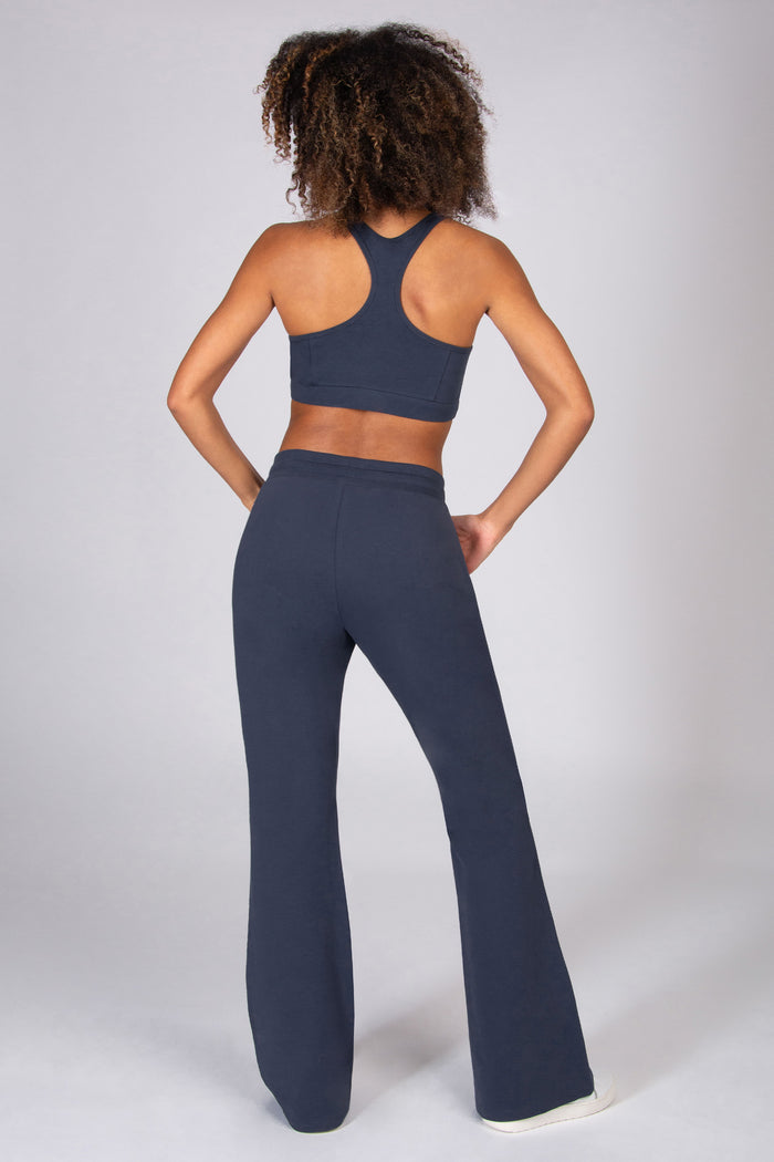 Woman wearing grey sports top and matching dark grey flared trousers on a light grey background.