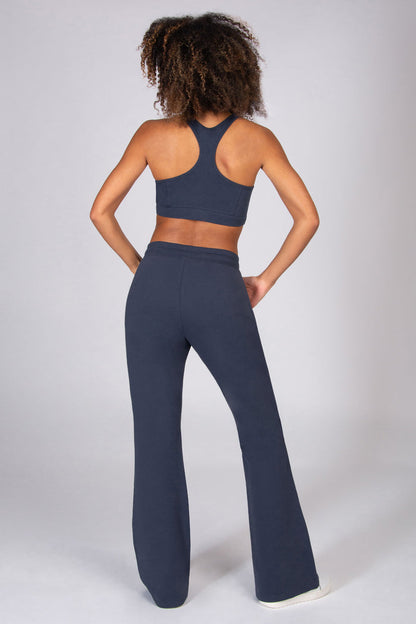 Woman wearing grey sports top and matching dark grey flared trousers on a light grey background.