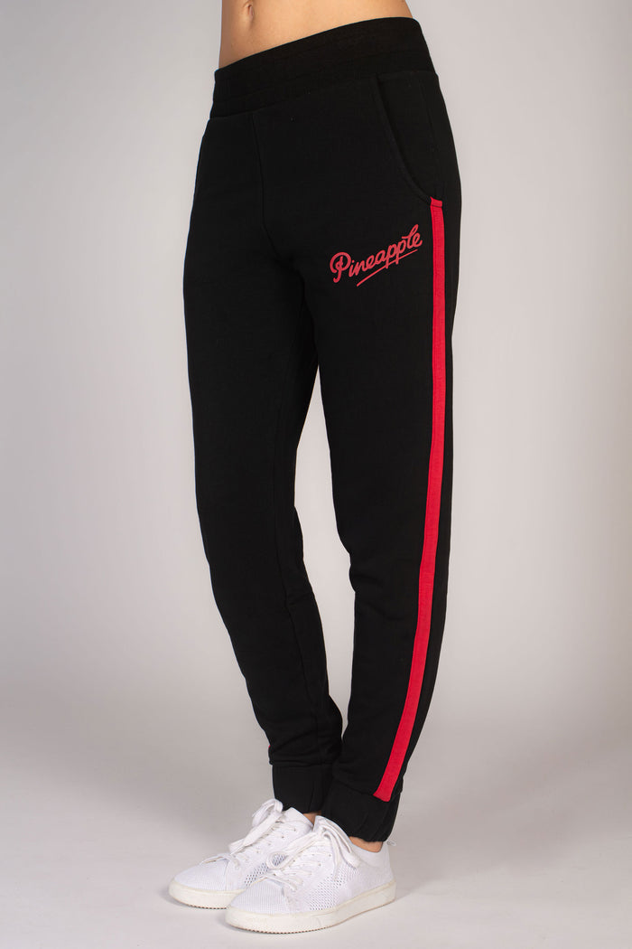 Women's black joggers with red stripe running down the leg. Large pockets and delicate Pineapple Dance Studios logo on hip.