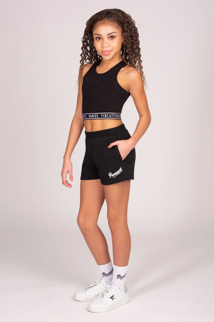 Girl wearing a black athletic outfit with pocket shorts on a light grey background