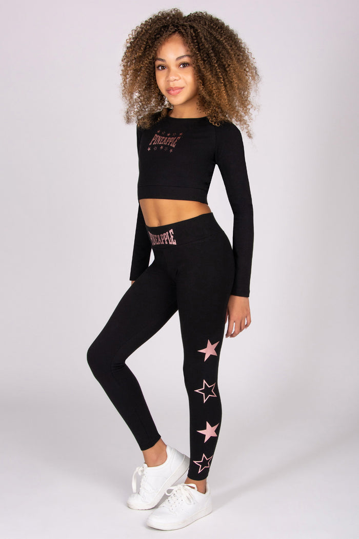 Skylar Blue wearing a black long-sleeve top and black leggings with pink star designs on a white background