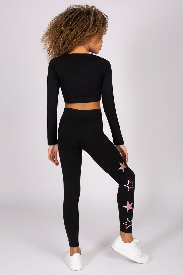 Girl wearing a black long-sleeve crop top and leggings with star patterns on a white background