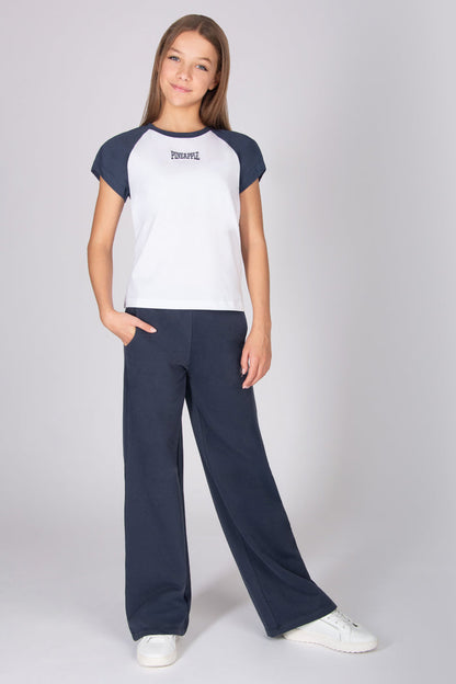Teenage girl wearing a white t-shirt with dark grey raglan sleeves with matching trousers on a grey background