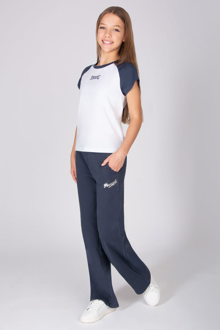 Teenage girl wearing a white and dark grey raglan sleeve t-shirt with wide leg trousers on a light grey background