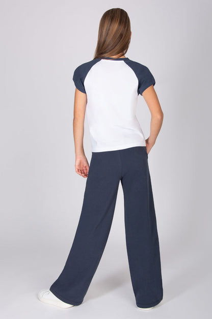Teenage girl wearing a white t-shirt with contrast dark grey raglan sleeves with navy wide leg trousers on a light grey background