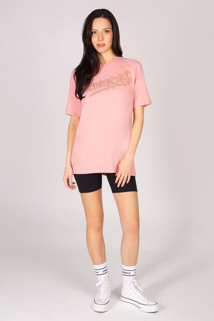 Woman wearing a pink oversized t-shirt, black shorts, and white sneakers on a light grey background