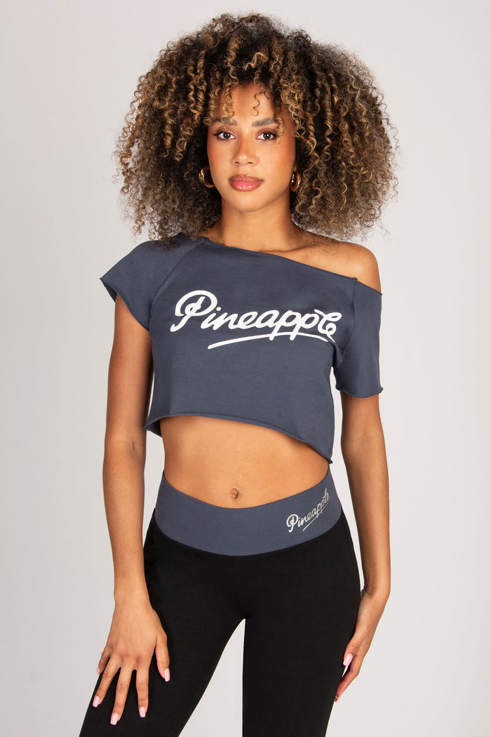 Woman wearing a dark grey off-shoulder top and black leggings with 'Pineapple' branding on a light grey background