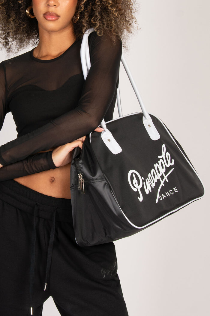 Person holding a black bag with 'Pineapple Dance' branding against a white background