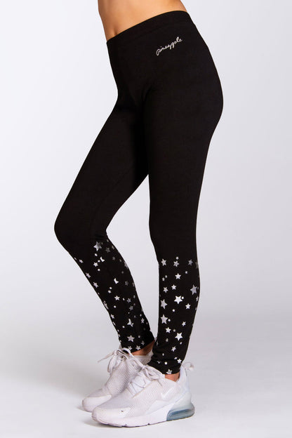 A person wearing black leggings with a silver foil star print and a sweatshirt, standing against a neutral background.