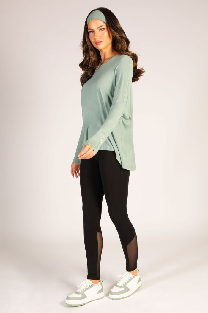Sage green long sleeve top in soft cotton-rich fabric, featuring a dipped back and small silver logo on the sleeve
