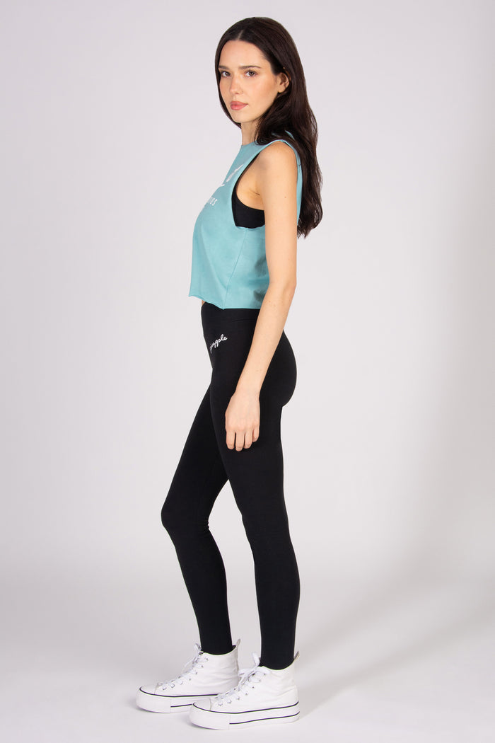 Woman wearing a light blue sleeveless top and black leggings on a white background