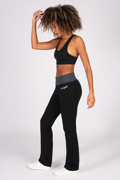Woman wearing a black sports bra and black flared leggings with a grey waistband on a white background