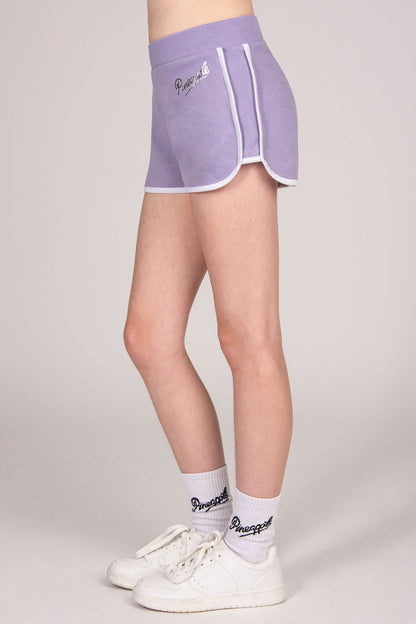 Person wearing a purple shorts with white trim and white sneakers on a plain background