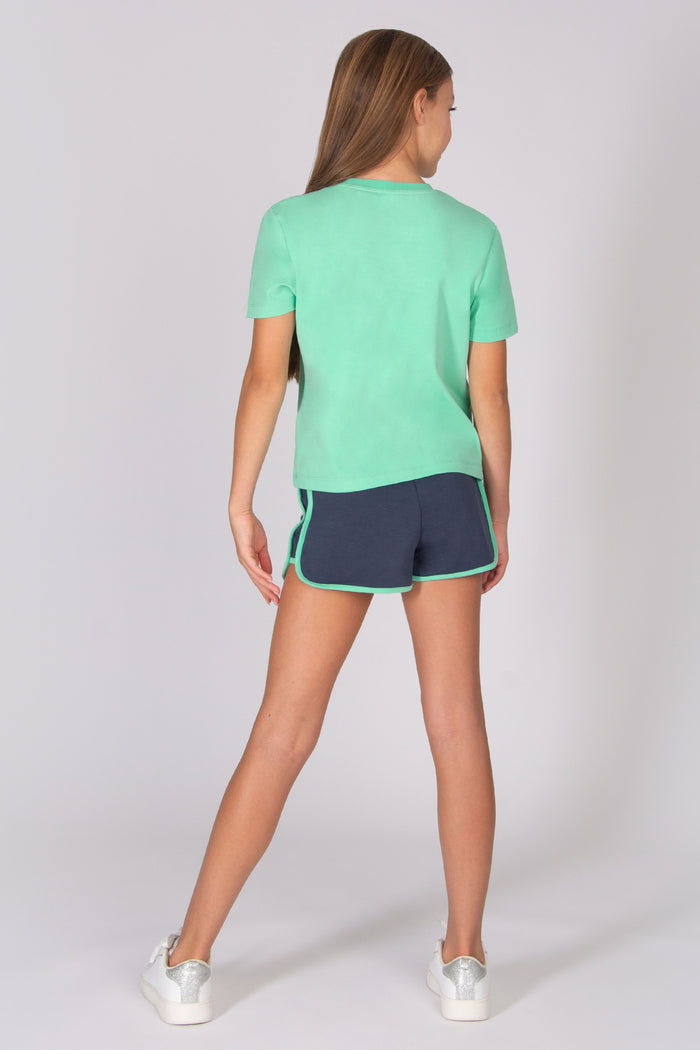 Teenager wearing a light blue t-shirt and dark grey shorts on a white background