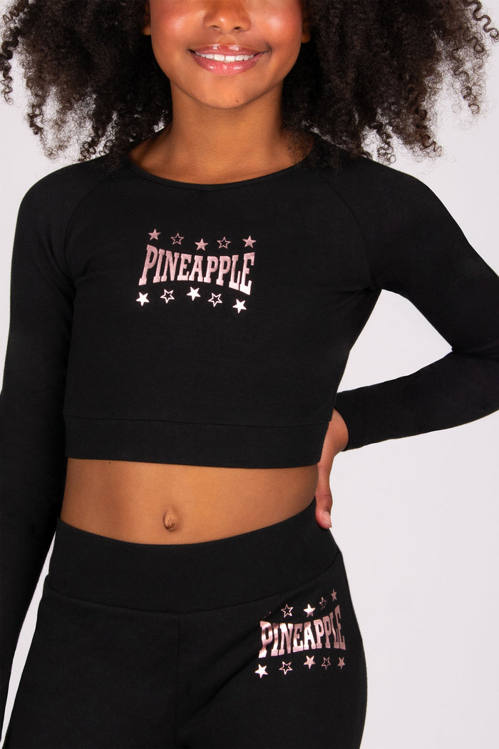 Girl wearing a black long-sleeve crop top and black leggings with 'Pineapple' branding on a plain background