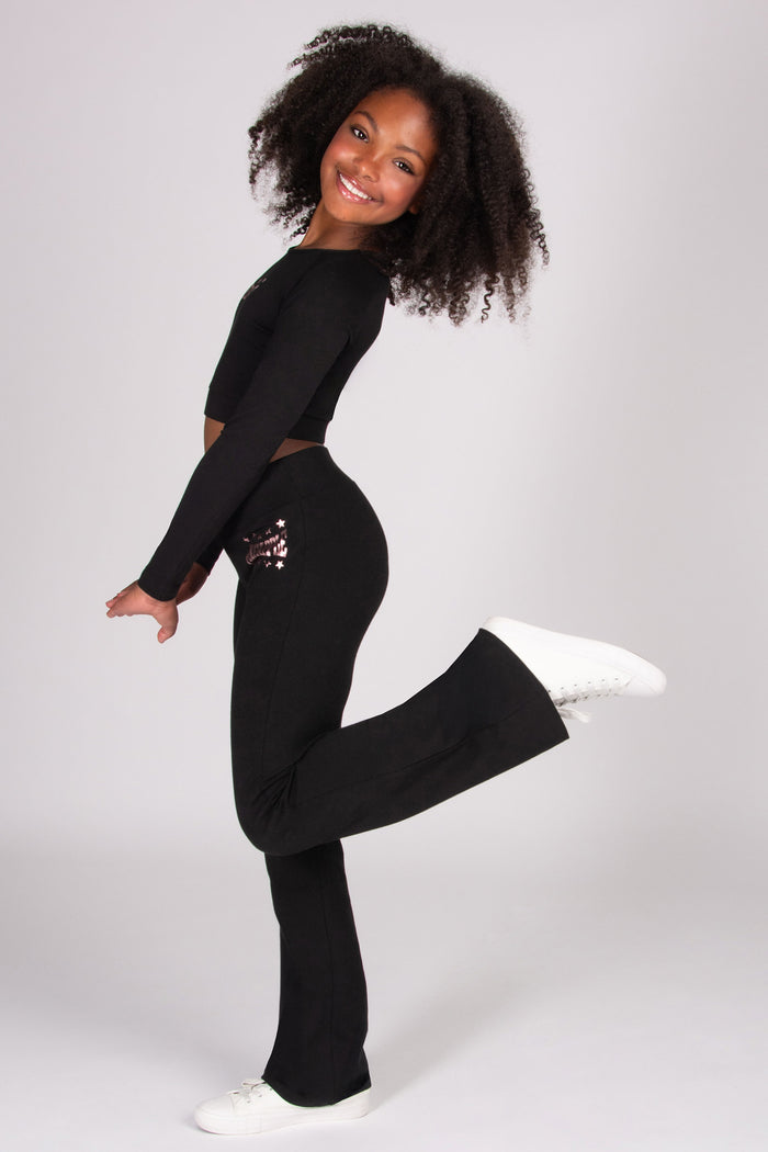 Girl wearing a black dance outfit with white shoes on a plain background