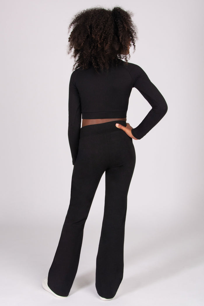Girl wearing a black long-sleeve top and black bootcut jersey trousers on a white background