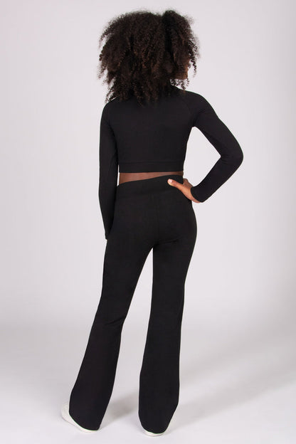 Girl wearing a black long-sleeve top and black bootcut jersey trousers on a white background
