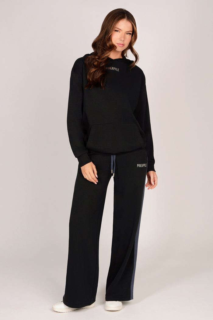 Woman wearing a black hoodie with black wide leg trousers on a light grey background