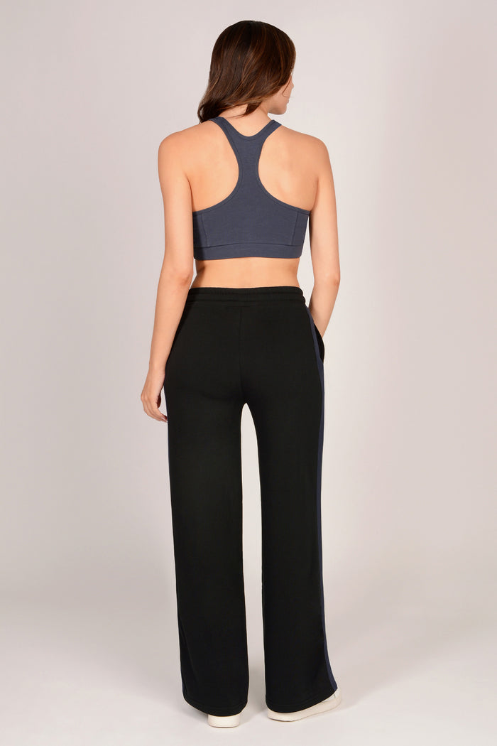 Woman wearing a dark grey sports bra and black trousers with dark grey drawcords and side panels on a light grey background