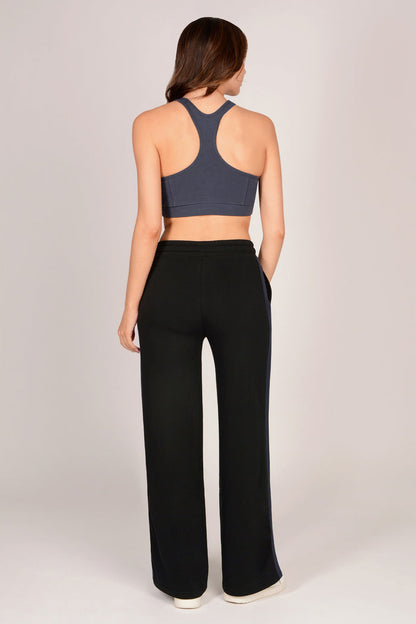 Woman wearing a dark grey sports bra and black trousers with dark grey drawcords and side panels on a light grey background