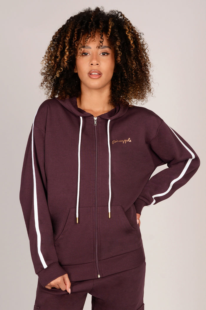 Woman wearing a maroon hoodie with white stripes on sleeve on a plain background