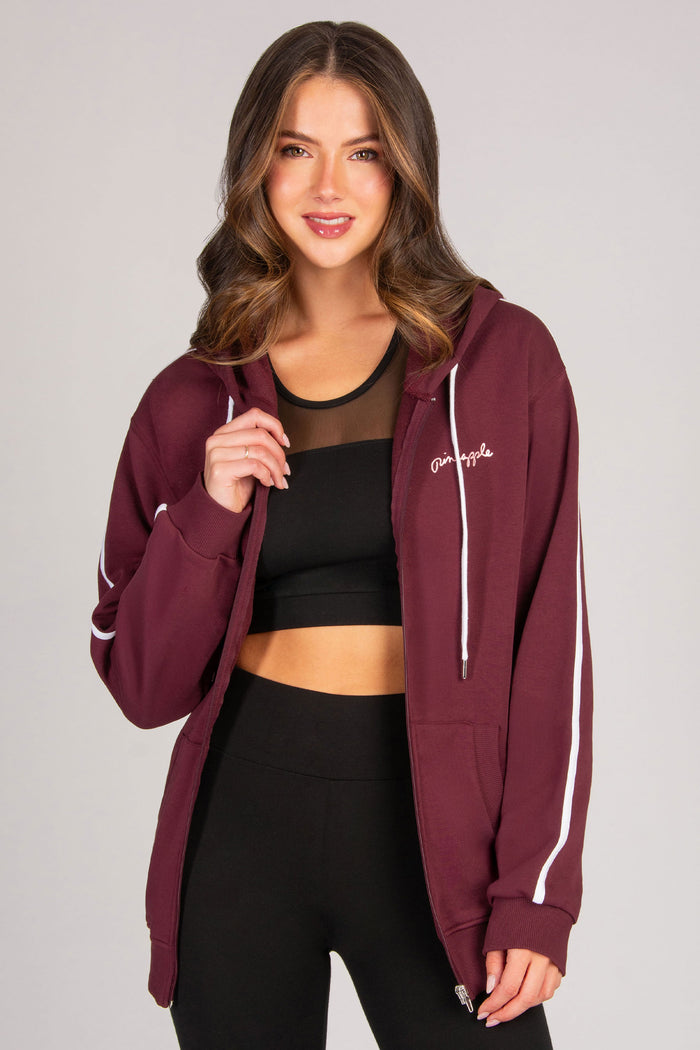 Woman wearing a maroon hoodie with white accents on a plain background