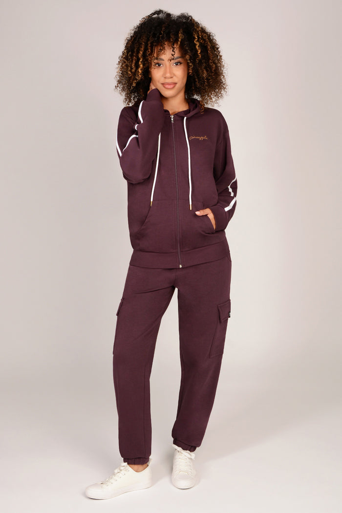 Woman wearing a maroon brown cargo joggers with matching zip hoodie on a plain background