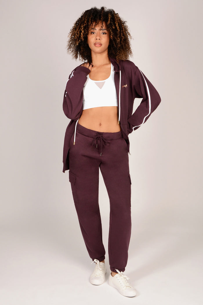 Woman wearing a maroon brown cargo joggers with white accents on a plain background