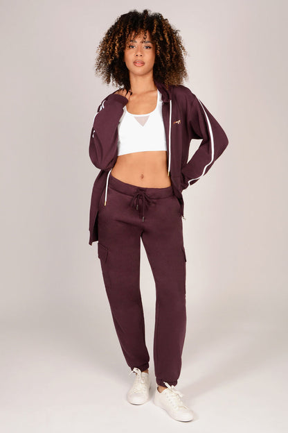 Woman wearing a maroon brown cargo joggers with white accents on a plain background