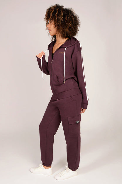 Woman wearing a maroon brown cargo joggers with matching zip hoodie on a plain background