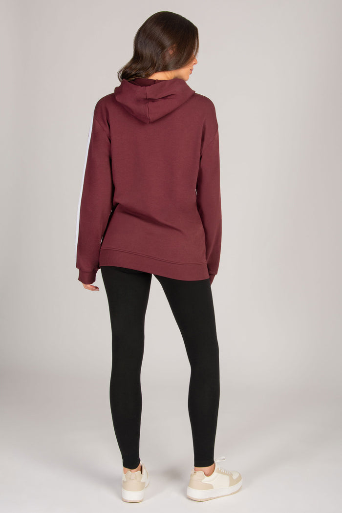 Woman wearing a burgundy hoodie and black leggings on a plain background