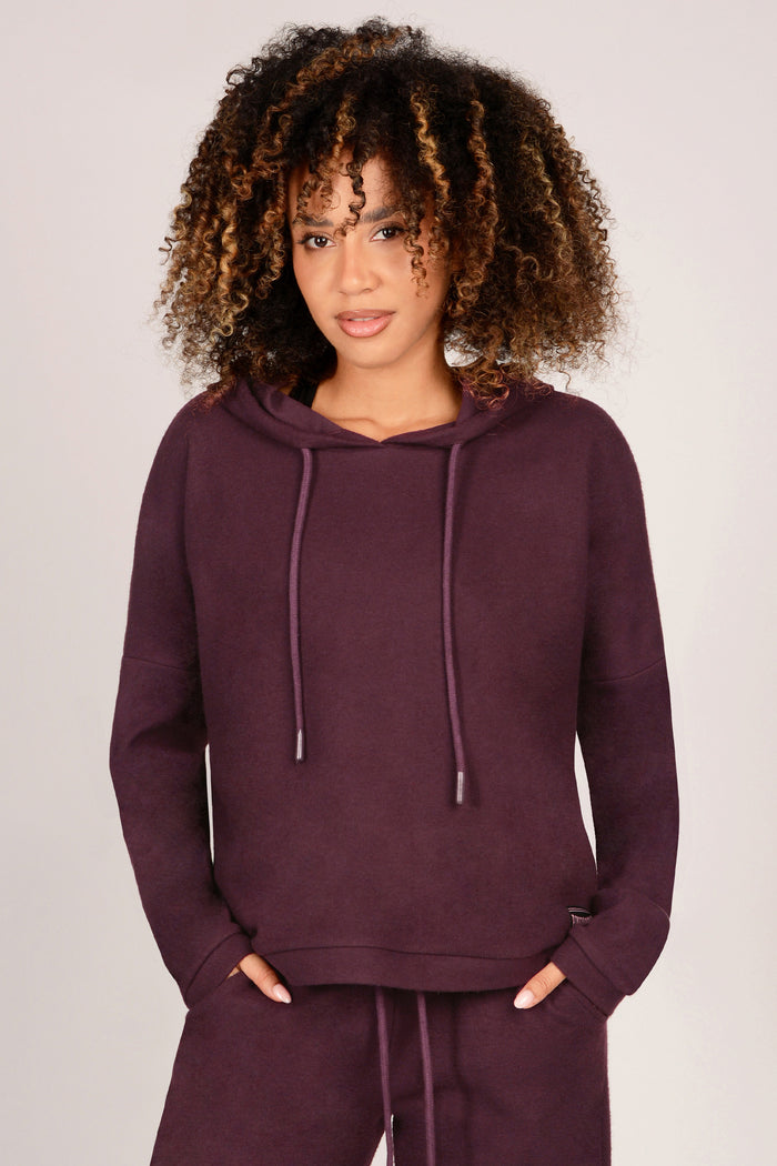 Woman wearing a maroon hoodie and matching trousers on a plain background