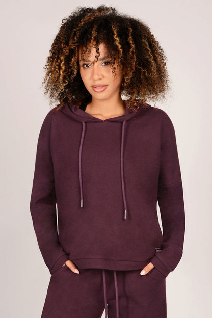Woman wearing a maroon hoodie and matching trousers on a plain background