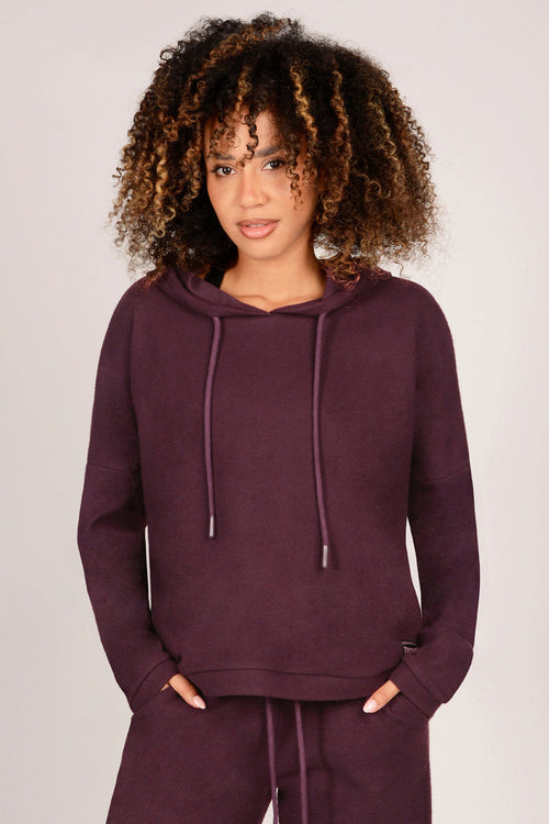 Woman wearing a maroon hoodie and matching trousers on a plain background